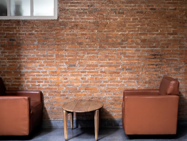 Sofá de cuero moderno de lujo marrón con vista lateral con mesa lateral redonda de madera decorada en un fondo de pared de ladrillo vacío Diseño interior de estilo loft con muebles y construcción de ladrillos