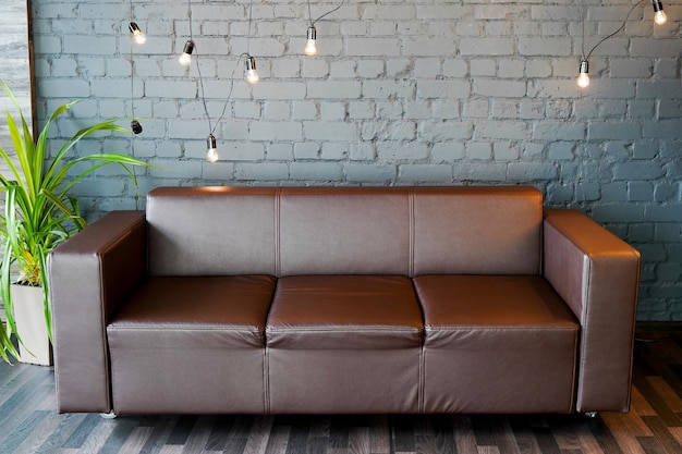 Sofá de couro marrom e parede de pedra com iluminação moderna, conceito de escritório interno