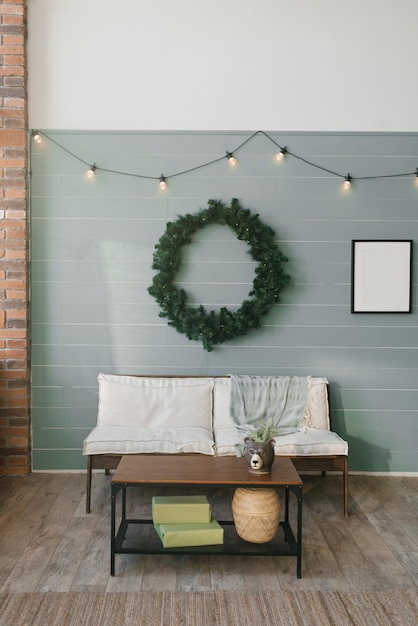 Sofá de madeira com almofadas macias brancas e uma grande guirlanda de Natal na parede forrada com ripa