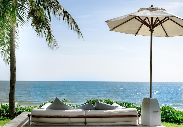 Sofa mit Blick auf Strand, Meer, Sonnenschirme, Kokospalmen und grünes Gras. blauer Himmel