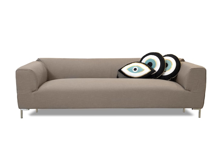 Foto sofá con patas de madera tapizado en tela beige marrón claro con cojines decorativos en forma de ojos sobre un fondo blanco
