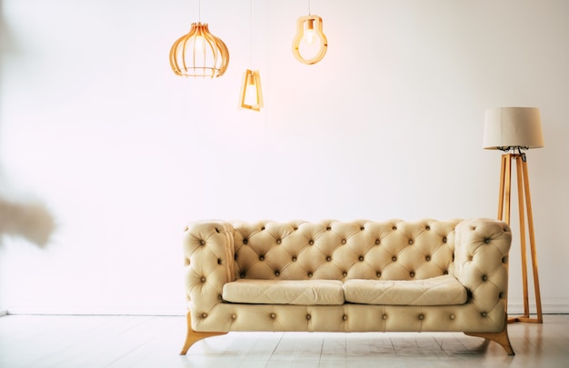 Sofá suave. Lámpara y sofá beige de pie contra una pared blanca en un moderno estudio.