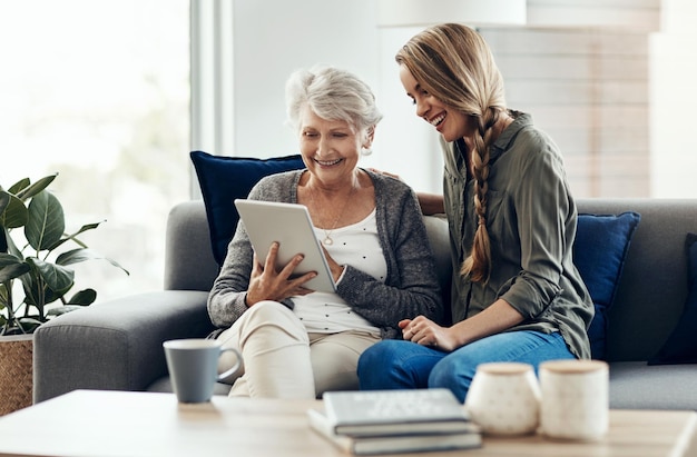 El sofá de la tableta y la mujer se relajan con la madre mayor en casa para obtener ayuda con el blog en línea, internet o conectividad. Sonrisa y persona mayor aprendiendo tecnología digital con la hija en casa.