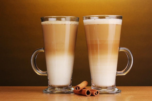 Soffee latte fragante en tazas de vidrio y canela en una mesa de madera con fondo marrón