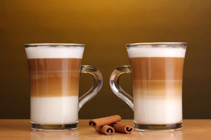 Foto soffee latte perfumado en tazas de vidrio y canela en una mesa de madera sobre un fondo marrón