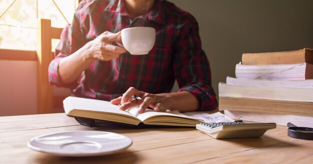 Foto soft focus blurclose-up homem asiático em camisa escocesa segurando café bebendo e lendo um livro