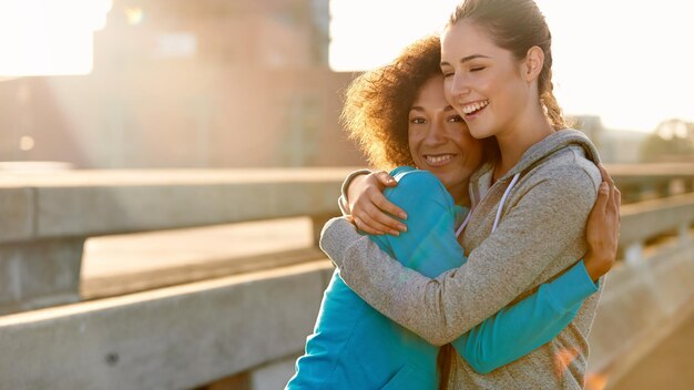 Sogar Joggen ist toll, wenn wir es zusammen machen Porträt zweier Joggerinnen, die sich umarmen und lachen, bevor sie durch die Stadt laufen