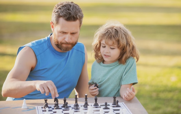 Sohn, der auf Gras liegt und Schach mit Vater spielt, konzentrierter kleiner Junge, der Schachstrategie entwickelt