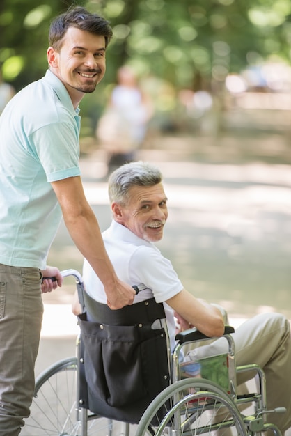 Sohn, der mit behindertem Vater im Rollstuhl am Park geht