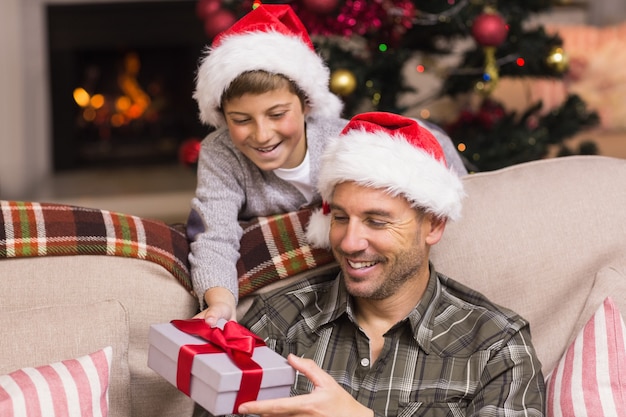 Sohn, der Vater ein Weihnachtsgeschenk auf der Couch anbietet