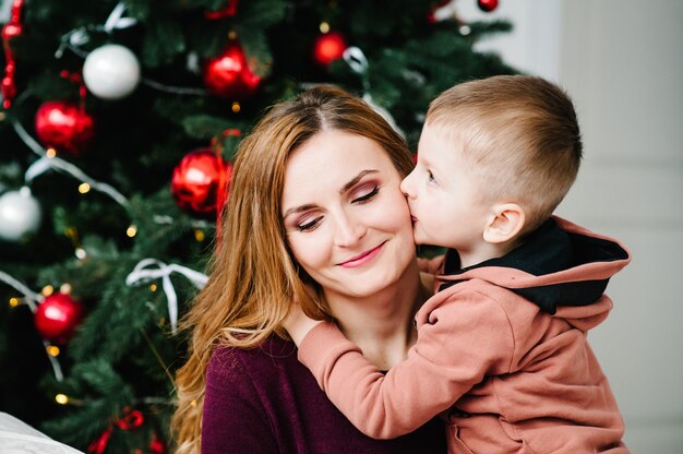 Sohn küsst Mama in der Nähe des Weihnachtsbaums Frohes neues Jahr und frohe Weihnachten