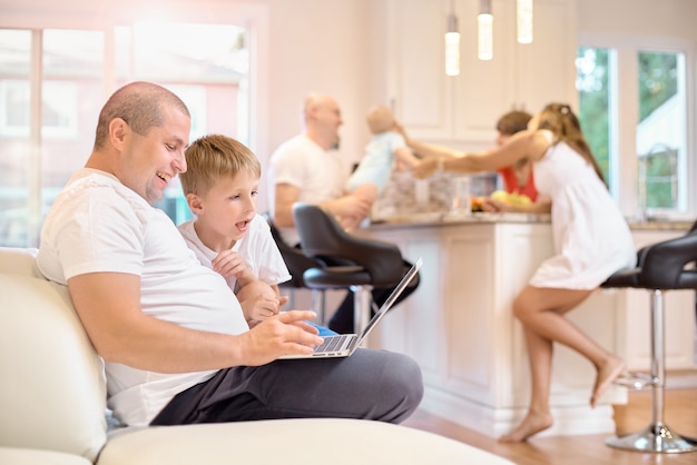 Sohn mit seinem Vater auf der Couch sitzen, Blick auf den Laptop, in der Küche Mutter Freunde und Baby