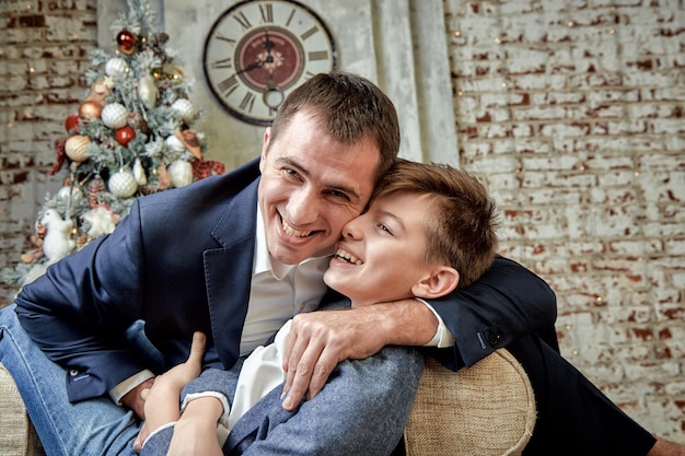 Sohn und Vater jubeln vor weihnachtlicher Dekoration Der Sohn und der Vater sitzen auf einem Stuhl und unterhalten sich fröhlich am Heiligabend