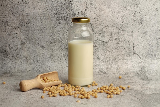 Sojamilchflasche und Sojabohnen mit einem Holzlöffel auf einer Marmorküchentheke