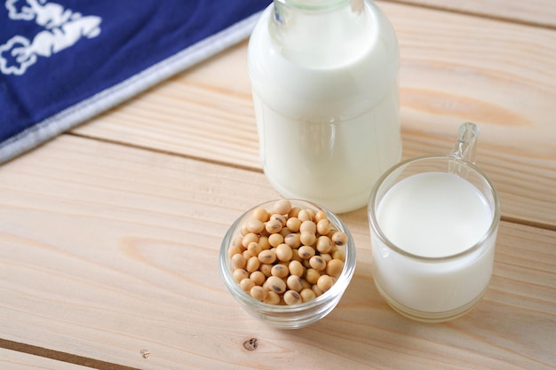 Sojasamen in Glasschale und Milch in Glasflasche auf Holztisch