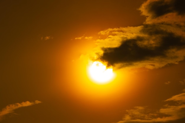 Un sol amarillo brilla a través de las nubes con la puesta de sol detrás de él.