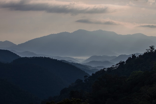 Sol brilhando através das nuvens com mountians recortadas