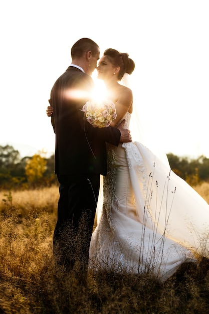 El sol brilla detrás de novios abrazándose en el campo