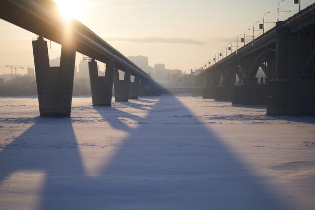 El sol brilla a través del puente de la ciudad sobre el río congelado en un día soleado