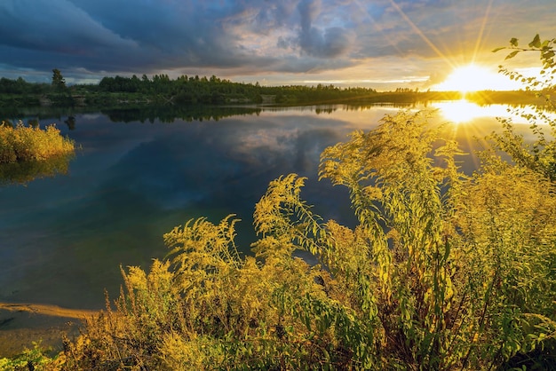 El sol brillante ilumina el cielo oscuro al atardecer y se refleja en el lago