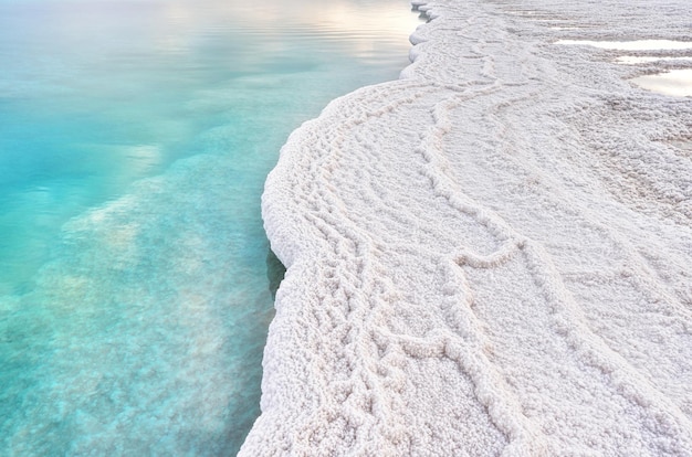 Sol da manhã brilha em cristais de sal branco, água calma verde ciano perto, paisagem típica na praia de Ein Bokek, Israel