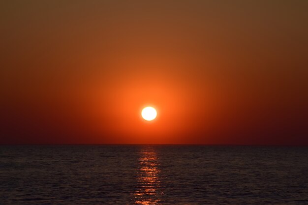 Sol da tarde carmesim contra o fundo do mar com reflexos nas ondas calmas