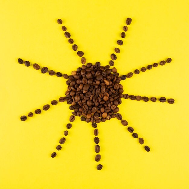 Foto el sol hecho de granos de café en amarillo. el concepto comienza la mañana con café. vista superior