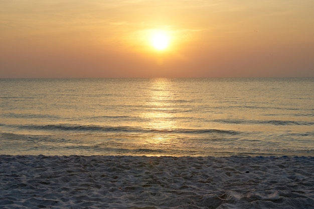 Foto sol no céu com mar e areia na praia com luz laranja quente