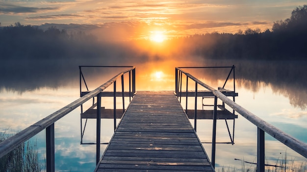 El sol sobre un lago brumoso con un muelle de madera en el bosque