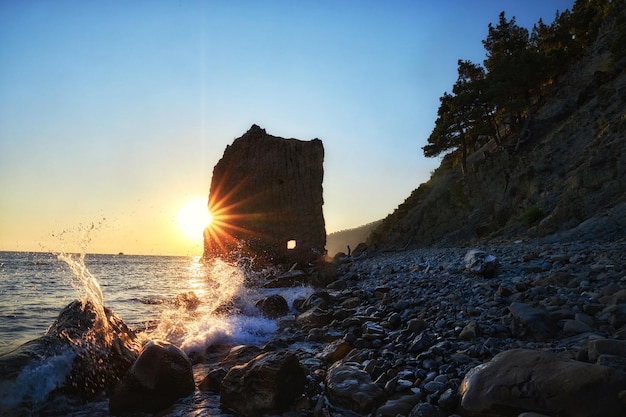 El sol se sumerge bajo el horizonte la costa rocosa la belleza de la naturaleza en la tranquilidad serena las olas golpean suavemente contra la orilla mientras los acantilados en silueta se paran majestuosamente contra el cielo oscuro