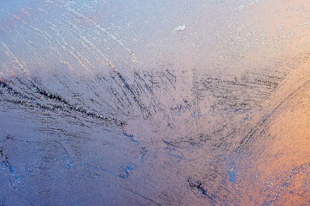 Sol vespertino y cielo azul brillante a través del patrón de escarcha en una ventana