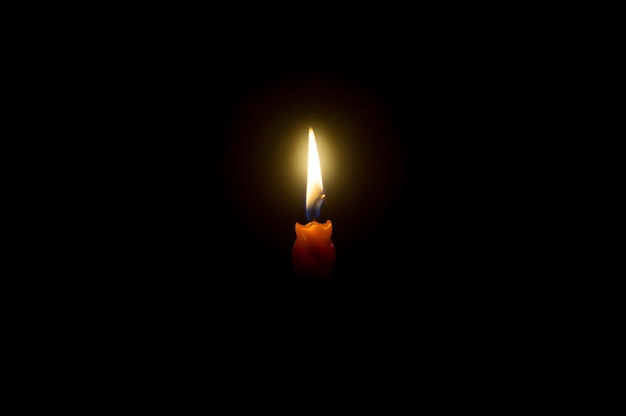 Una sola llama de vela encendida o luz brilla en una vela naranja en espiral sobre fondo negro