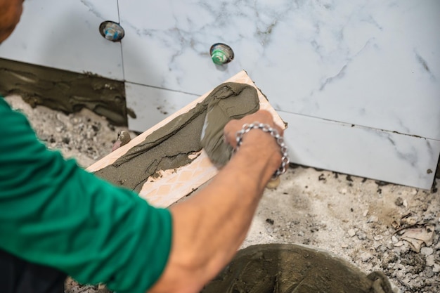 Solador macho con llana colocando baldosas de mármol con cemento en el baño Desarrollo de viviendas Renovación de mejoras interiores