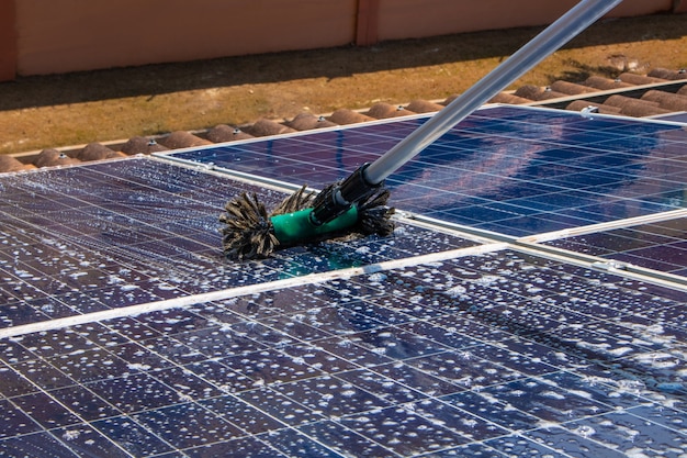 Solararbeiter, der Photovoltaikmodule mit Bürste und Wasser säubert. Photovoltaik-Reinigung.