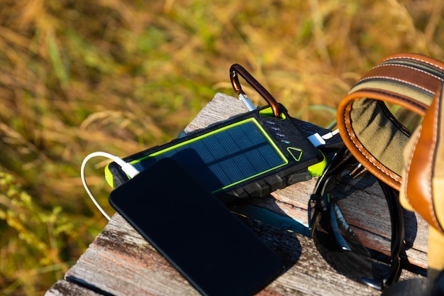 Foto solarenergie-batteriegerät, powerbank und telefon auf einem holztisch mit rucksack. laden sie ihr smartphone mit solarenergie auf. selektiver fokus