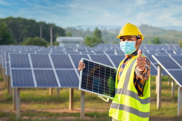 Solarenergietechniker stehend, Solarzellen haltend und Daumen hoch, Solarzellenpanel mit starker Sonne.