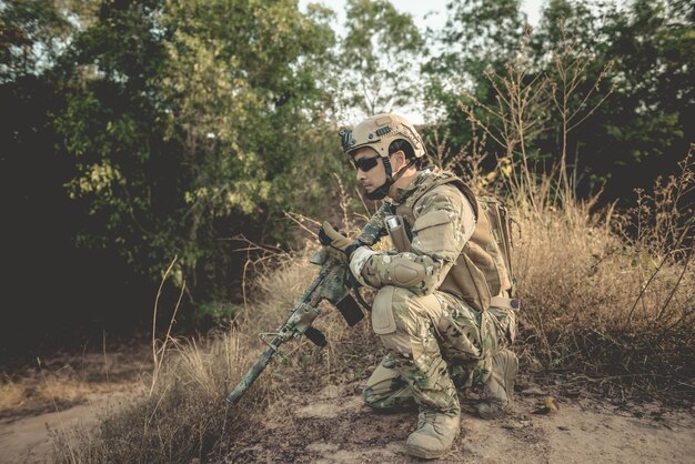 Un soldado con un arma se había sentado en el bosque. Está usando un walkie-talkie para pedir refuerzos militares en concepto de guerra.