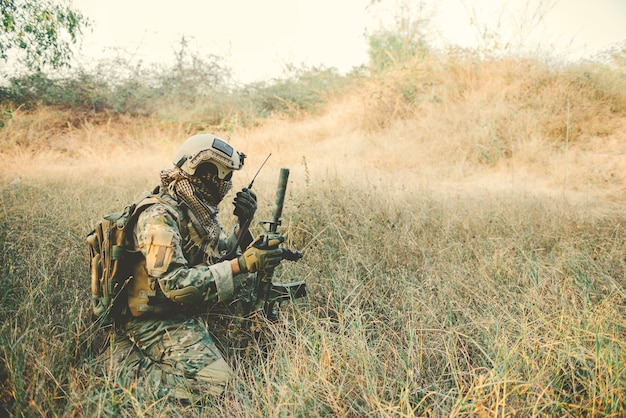 Un soldado con un arma se había sentado en el bosque. Está usando un walkie-talkie para pedir refuerzos militares en concepto de guerra.