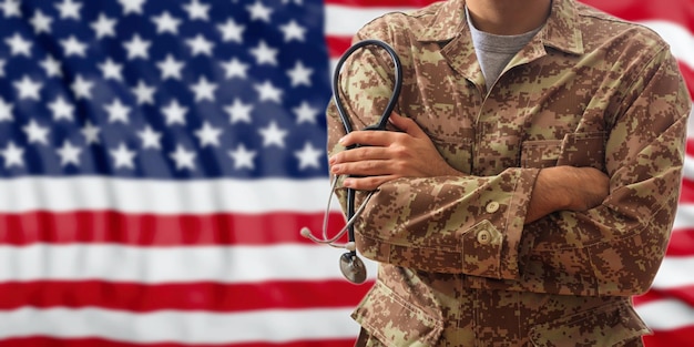 Foto soldado com estetoscópio em um uniforme militar americano em pé sobre um fundo de bandeira dos eua