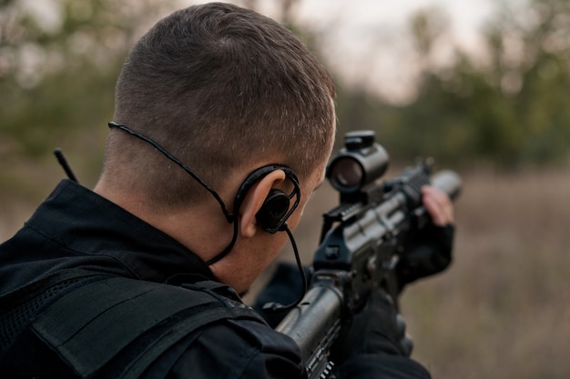 Soldado da força especial em uniforme preto apontando um rifle de assalto