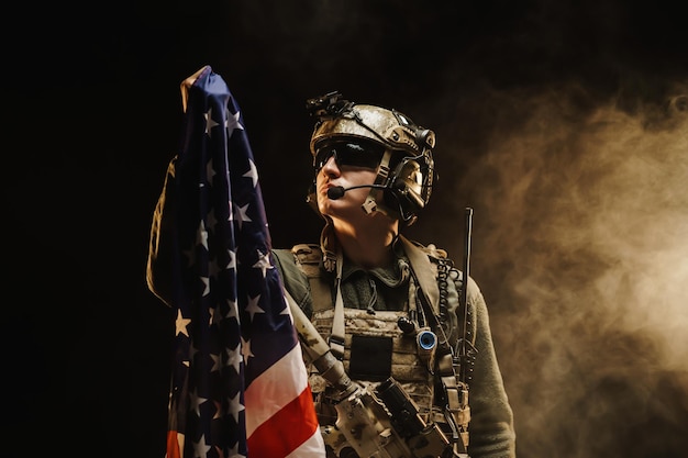 Soldado das forças especiais segurando a bandeira nacional dos Estados Unidos no escuro