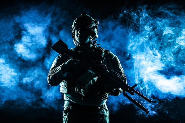 Soldado do exército em uniformes de combate com metralhadora, porta-placas e capacete de combate. Foto de contorno de estúdio, luz de fundo, fundo escuro de fumaça brilhante