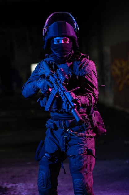 Soldado do exército em uniformes de combate com um rifle de assalto e fundo escuro de missão noturna de capacete de combate. Efeito de luz em gel azul e roxo. Foto de alta qualidade