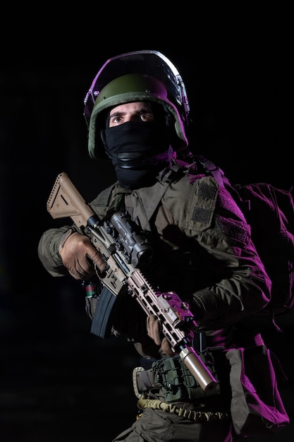 Soldado do exército em uniformes de combate com um rifle de assalto e fundo escuro de missão noturna de capacete de combate. Efeito de luz em gel azul e roxo. Foto de alta qualidade