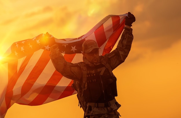 Foto soldado del ejército sosteniendo en alto la bandera estadounidense contra el cielo durante la puesta de sol