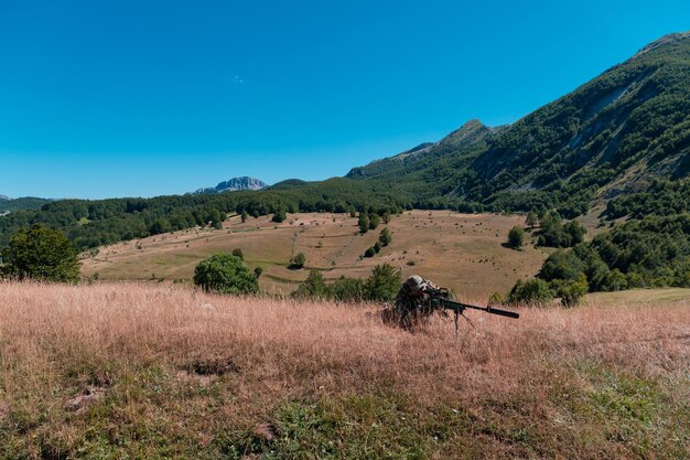 Soldado del ejército sosteniendo un rifle de francotirador con alcance y apuntando en el bosque. Concepto de guerra, ejército, tecnología y personas.