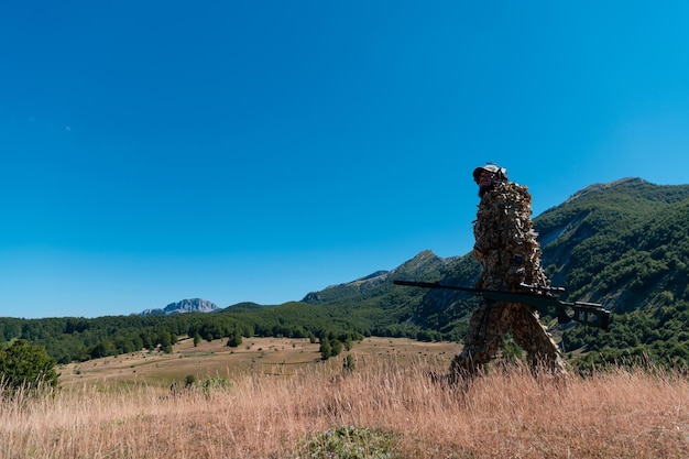 Soldado del ejército sosteniendo un rifle de francotirador con mira y caminando por el bosque. concepto de guerra, ejército, tecnología y personas.