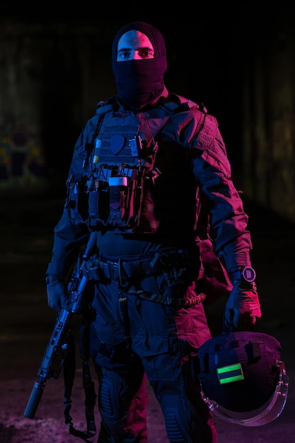 Soldado del ejército con uniformes de combate con un rifle de asalto y un casco de combate en una misión nocturna de fondo oscuro. Efecto de luz de gel azul y morado. Foto de alta calidad