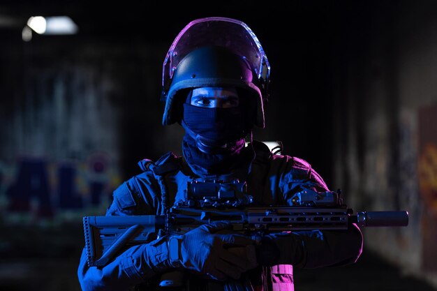 Soldado del ejército con uniformes de combate con un rifle de asalto y un casco de combate en una misión nocturna de fondo oscuro. Efecto de luz de gel azul y morado. Foto de alta calidad