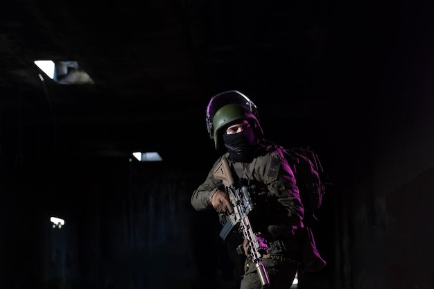 Soldado del ejército con uniformes de combate con un rifle de asalto y un casco de combate en una misión nocturna de fondo oscuro. Efecto de luz de gel azul y morado. Foto de alta calidad